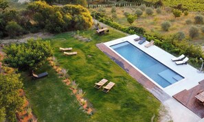 Eine Vogelperspektive auf einen modernen Poolbereich mit einem rechteckigen Pool, mehreren Liegestühlen und einer Holzterrasse.