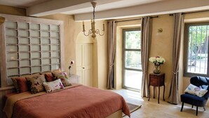 A bedroom with a large bed, a chandelier, a window with curtains, and a chair. - Former silk mill at the foot of Mont Ventoux (Crestet)