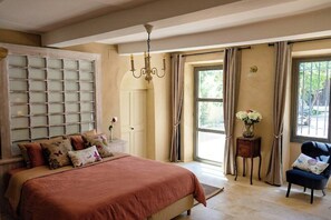 Ein Schlafzimmer mit einem großen Bett, einer Pendelleuchte, einem Fenster mit Vorhängen und einem Sessel.
