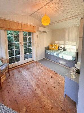 A bedroom with a bed, a desk, a chair, and a window with a view of greenery.