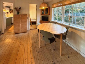 A wooden dining table with chairs, a television, and a window with a view of trees.