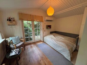 A bedroom with a bed, a chair, a window with blinds, and a hanging light fixture.