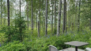 A wooden deck with a table and two chairs, surrounded by dense greenery and tall trees. - Timeless home with nature at your doorstep (Arvika)