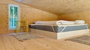 A wooden cabin bedroom with a bed, a window, and a yellow chair. - Timeless home with nature at your doorstep (Arvika)