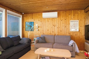 Ein Zimmer mit Holzwänden, einer Couch, einem kleinen Tisch, einer Wand-Klimaanlage und einem Fernseher.