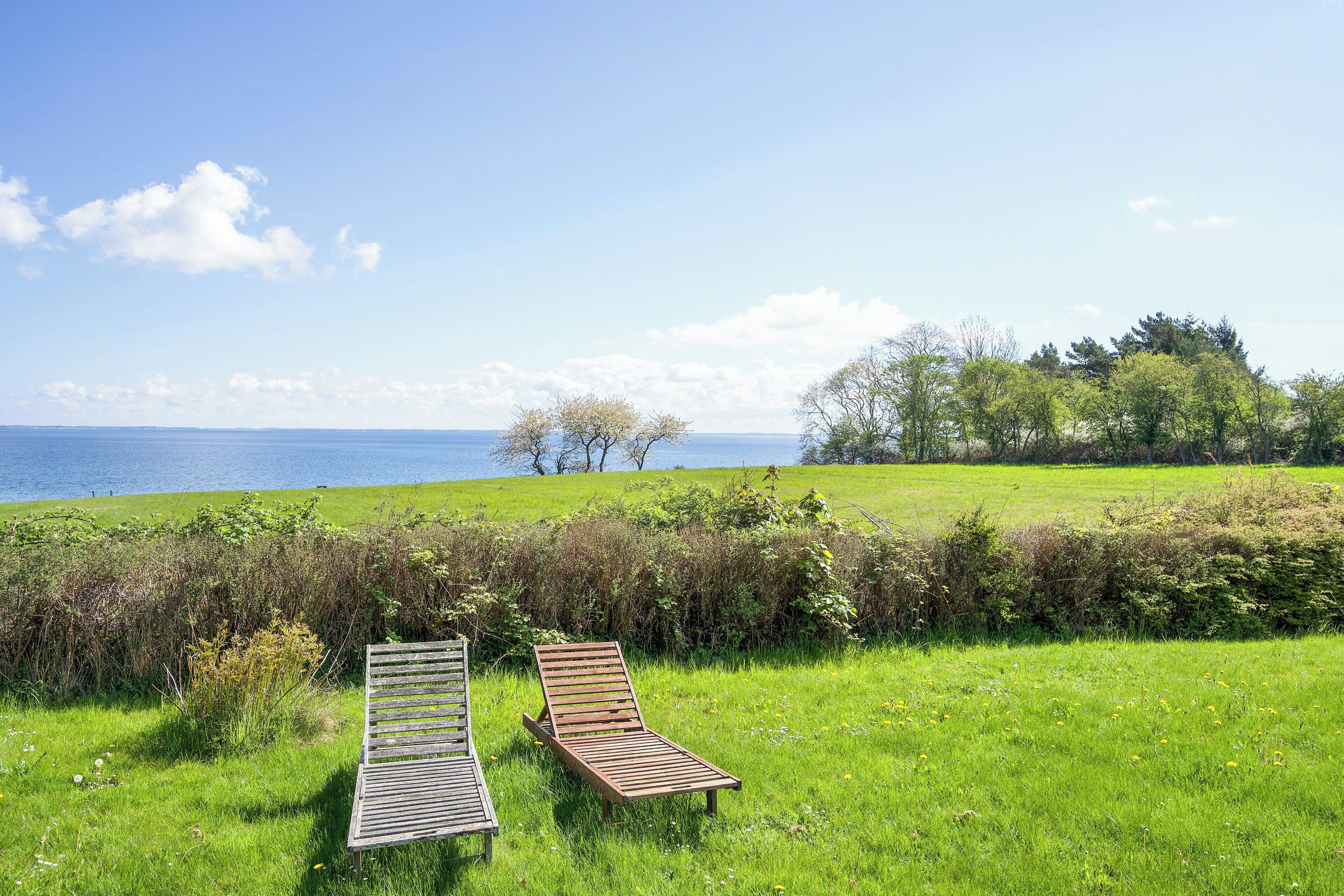 A grassy field with two wooden loungers facing a body of water.
