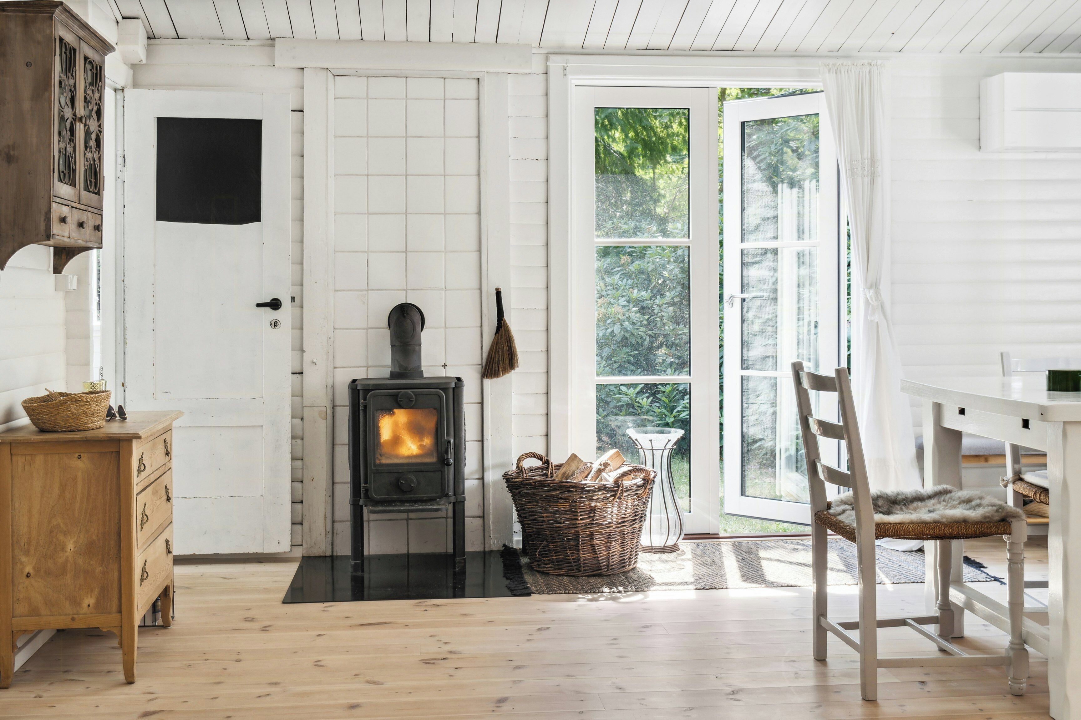 A room with a wood-burning stove, a wicker basket, a wooden dresser, and a chair.