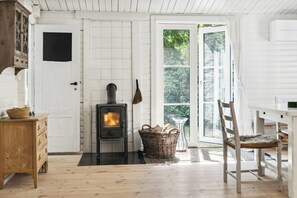 Una habitación con estufa de leña, una cesta de mimbre, un aparador de madera y una silla.