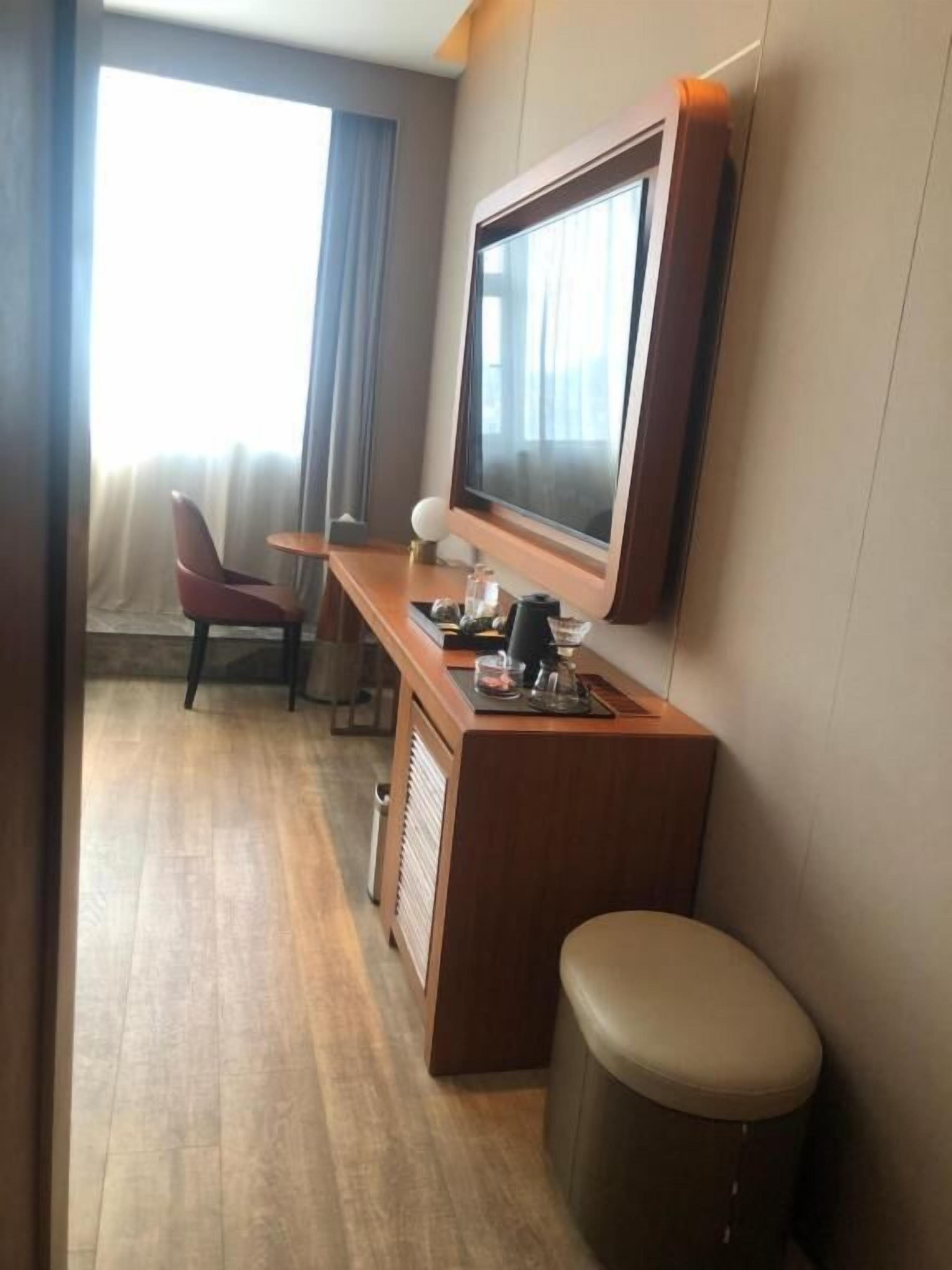 Ein kleines Hotelzimmer mit einem Holztisch, einem Fernseher, einem Stuhl und einem kleinen Hocker.