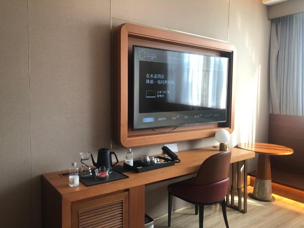 Ein Hotelzimmer mit einem großen Flachbildfernseher an der Wand, einem Holztisch mit Stuhl, einem kleinen runden Tisch und einer Couch.