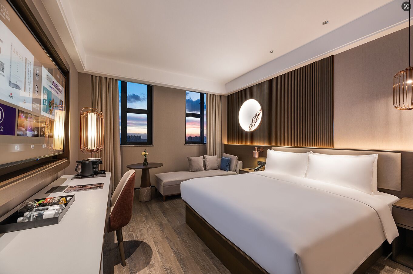 Une chambre d’hôtel avec un grand lit, un bureau avec une chaise, une petite table ronde et une vue sur la ville par les fenêtres.