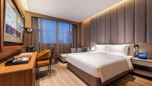 Une chambre d’hôtel moderne équipée d’un grand lit, d’un bureau, d’une chaise, d’une machine à café et d’un panneau de commande numérique.