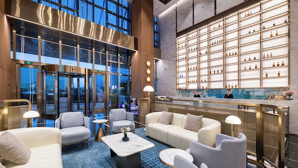Un hall d’hôtel doté d’un bar, de coins salon et offrant une vue sur l’extérieur grâce à de grandes fenêtres.