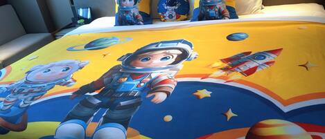 A bed with a space-themed bedspread, pillows, and a nightstand with a lamp.
