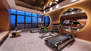 Une salle de sport équipée de tapis de course, d’un banc et d’un miroir.