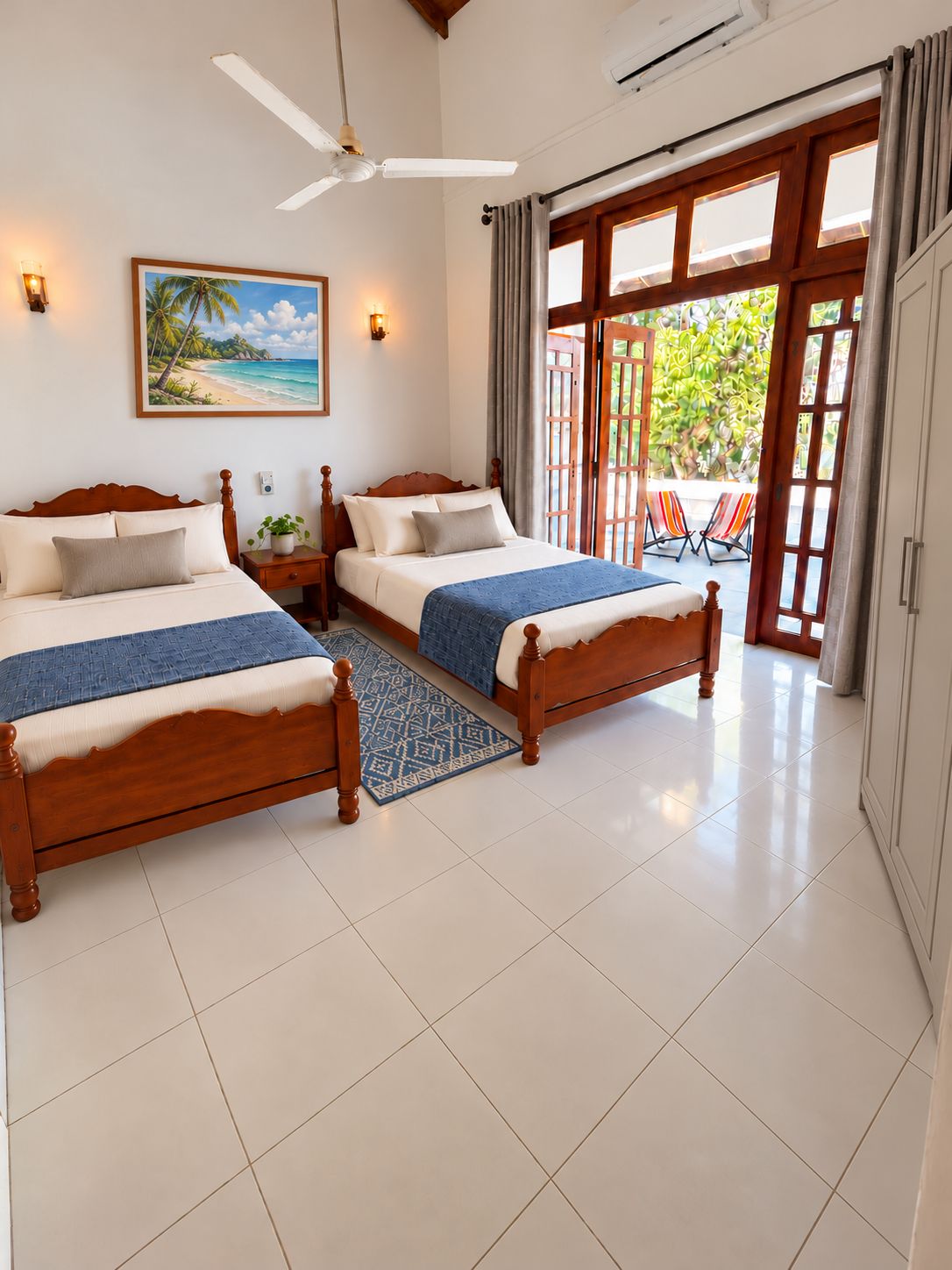 A hotel room with two wooden beds, a ceiling fan, a beach-themed painting, and a view of the outdoors through a glass door.