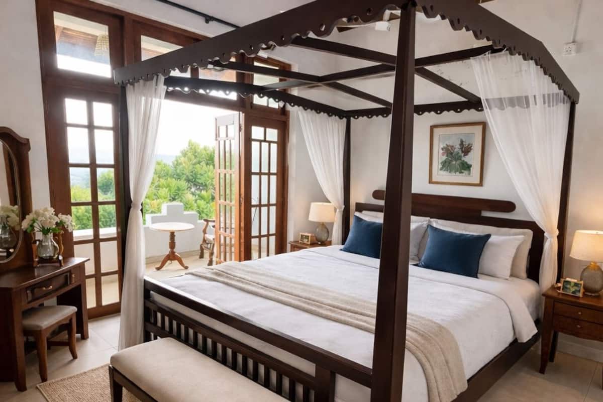 A four-poster bed with a canopy, a bench, a desk, and a chair in a room with a view.