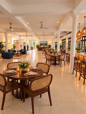 A spacious hotel lobby with a central dining area, multiple seating arrangements, and a bar. - Dimora Ceylon (Dikwella)