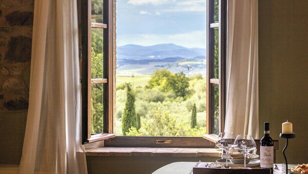 Ein Zimmer mit offenem Fenster, einem Tisch mit Weingläsern, einer Flasche und einer Kerze.