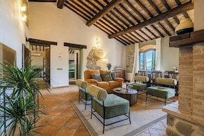 A spacious living area with a stone fireplace, a sofa set, and a dining area with a view. - Private pool villa on wine estate near Montalcino (Grosseto)