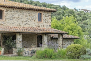A stone building with a tiled roof, a porch with chairs, and a small table. - Private pool villa on wine estate near Montalcino (Grosseto)