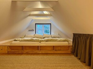 Ein Schlafzimmer mit schrägem Dach, einem Fenster, einem Bett mit gestreifter Bettwäsche und einem Holz-Kopfteil.