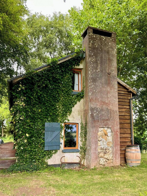 Un bâtiment rustique avec une cheminée en pierre, des murs couverts de lierre et une porte en bois.
