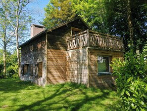 Un chalet en bois rustique doté d’un balcon, entouré d’une végétation luxuriante.