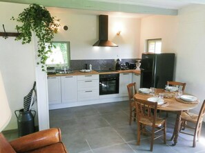 Une cuisine moderne avec des meubles blancs, une cuisinière noire et un coin repas comprenant une table et des chaises en bois.
