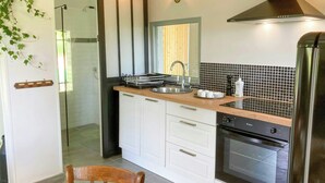 A modern kitchen with a built-in oven, a stainless steel sink, and a black tiled backsplash. - Cottage in château grounds near Rouen (Limésy)