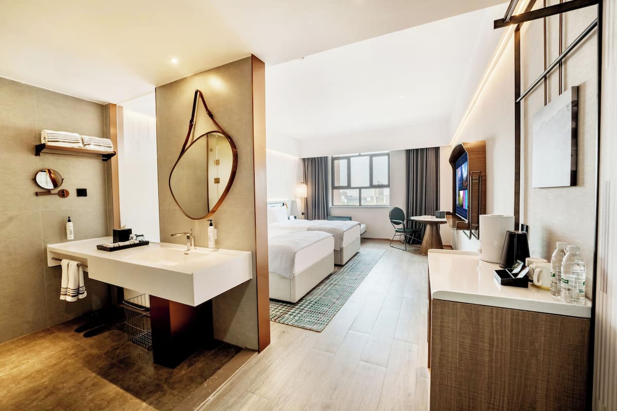 Una habitación de hotel moderna con un amplio tocador, una cama, un escritorio y un espejo grande.