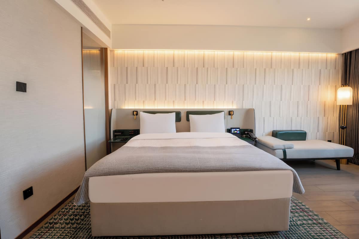 Una habitación de hotel moderna con una cama grande, mesitas de noche, un escritorio y un rincón de descanso.