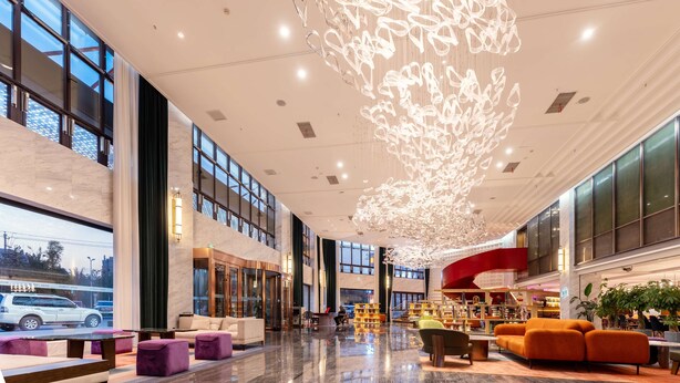 A spacious lobby with a modern chandelier, seating areas, and large windows.