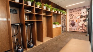 A hotel room with a wooden floor, a bench, a wall-mounted washing machine, and a shelf with potted plants.