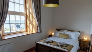 Un dormitorio con cama de madera, vista al mar a través de una ventana, mesita de noche con lámpara y radiador.