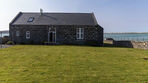 Una casa de piedra con un césped y vista al mar.