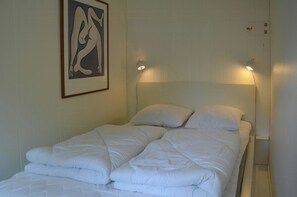Ein ordentlich bezogenes Bett mit weißer Bettwäsche, ein gerahmtes Kunstwerk an der Wand und zwei Wandleuchten.