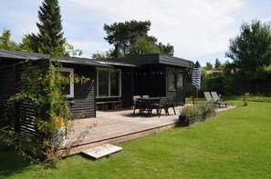 Eine moderne Holzhütte mit Terrasse, Sitzgelegenheit im Freien und Blick auf die umliegende Natur.