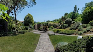 Ein Gartenweg führt zu einem Gebäude mit modernem Design, umgeben von verschiedenen gepflegten Sträuchern und Bäumen.