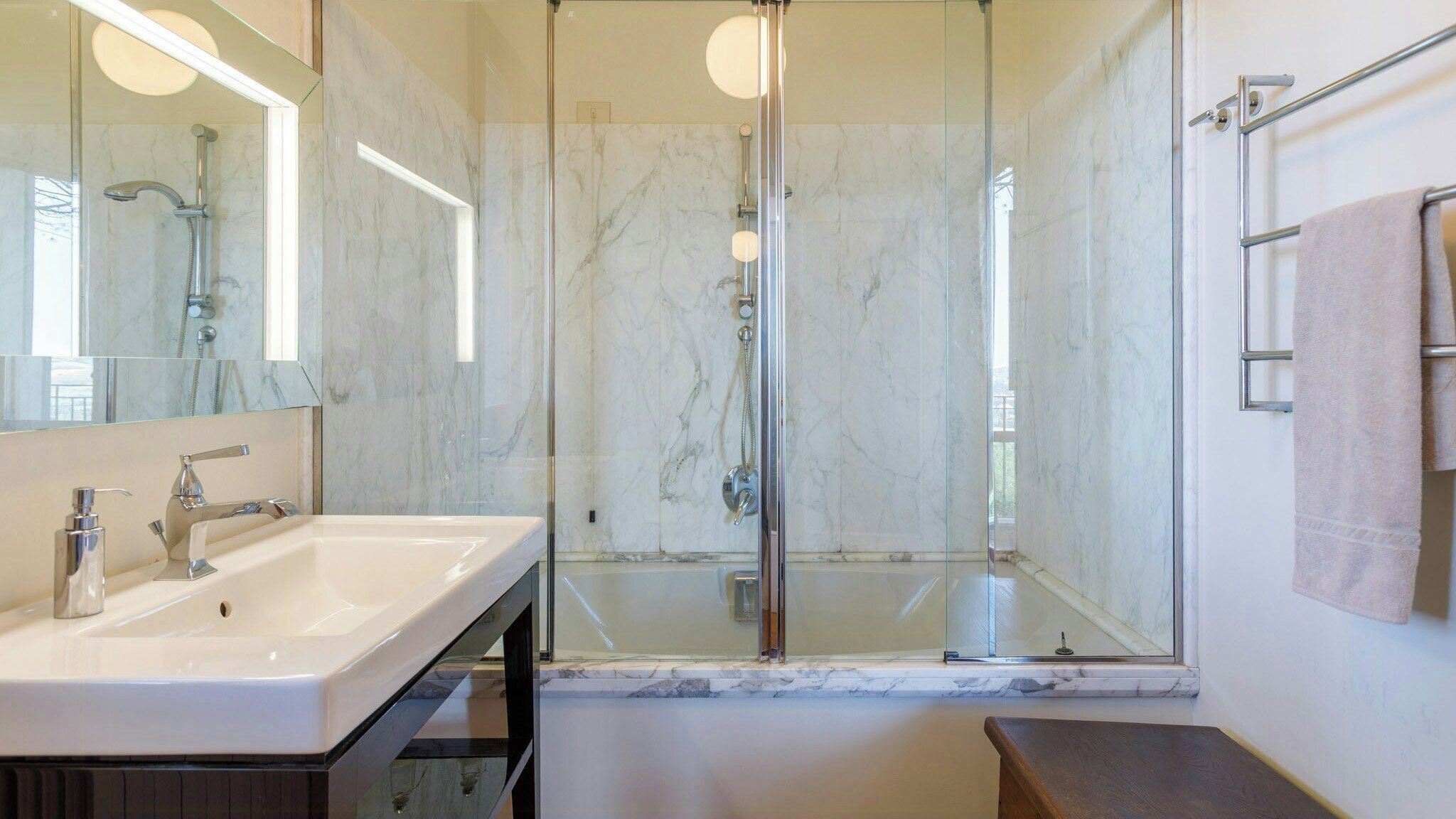 Uma casa de banho moderna com chuveiro em cabine de vidro, um lavatório branco com espelho e um porta-toalhas.
