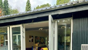 Une maison moderne dotée d’une terrasse, d’un barbecue et d’une porte-fenêtre coulissante donnant sur un espace de vie comprenant un canapé et une table.