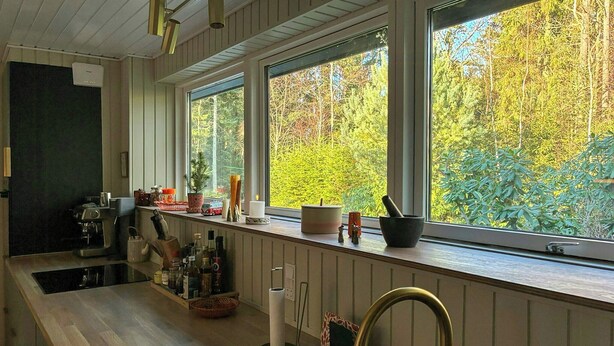Une cuisine dotée d’un plan de travail en bois, d’un évier et d’une fenêtre donnant sur une forêt.