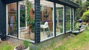 Une véranda dotée de grandes portes vitrées, d’une façade en bois et donnant sur un jardin.