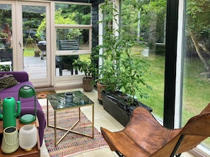 Een zonnig terras met een paarse bank, een leren fauteuil, een glazen tafel en potplanten.