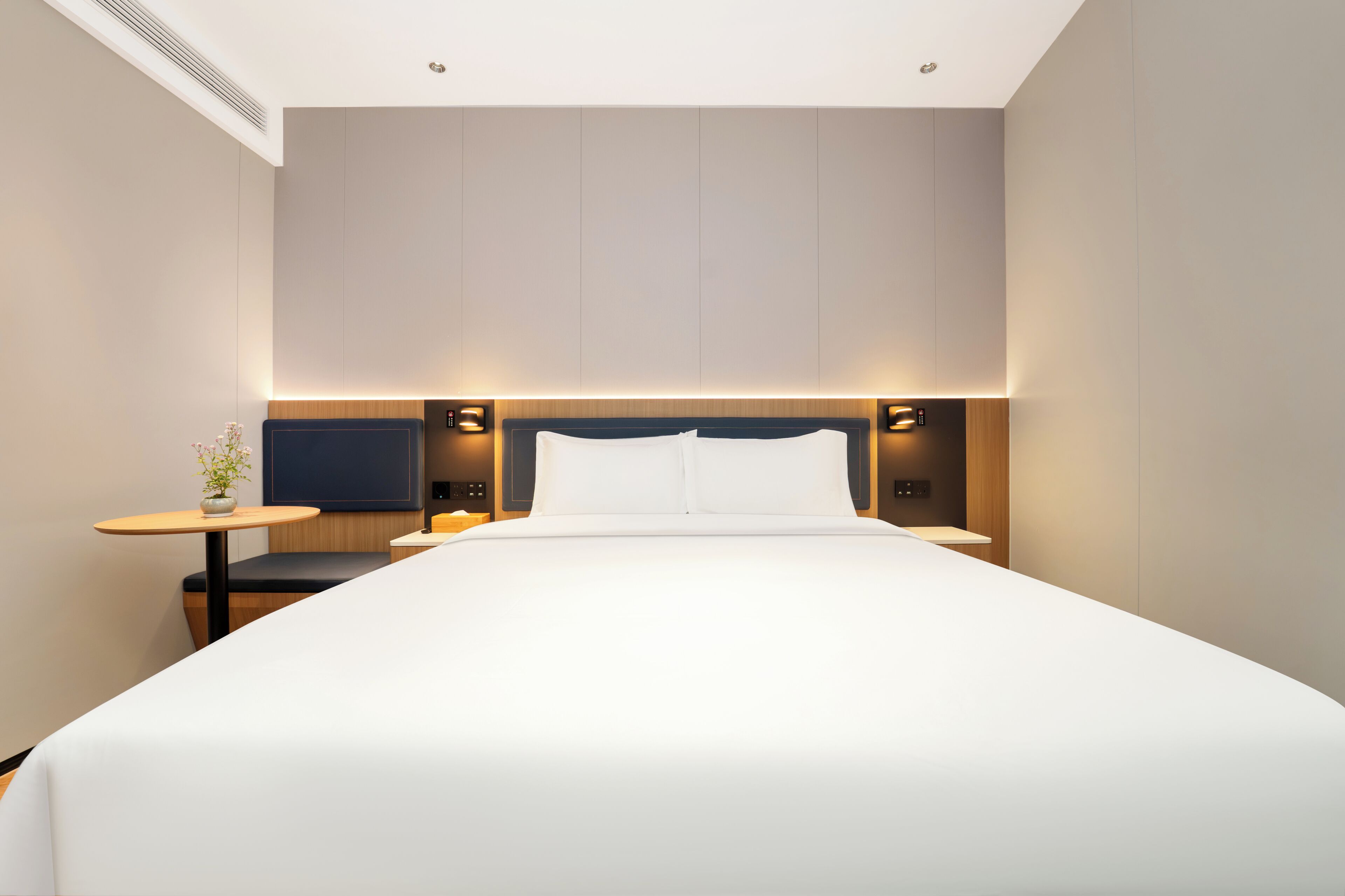 A modern hotel room with a large bed, bedside tables, and a flat-screen TV.