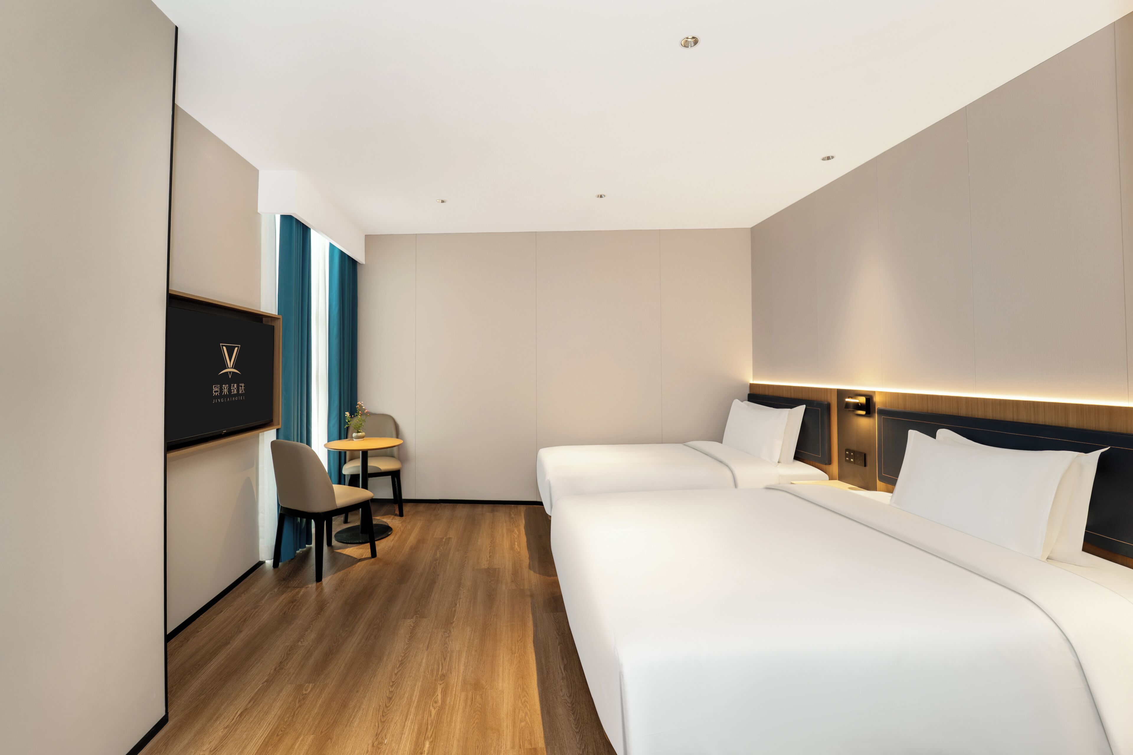 Quarto de hotel com chão de madeira, uma cama, uma escrivaninha com cadeira e televisão na parede.