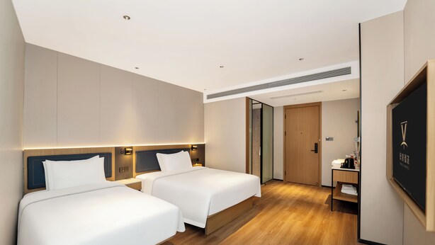 A hotel room with two beds, a desk, a mirror, and a door.