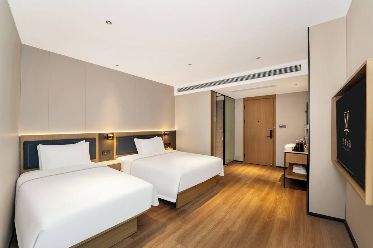 Una habitación de hotel con dos camas, un escritorio, un espejo y una puerta.