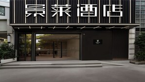 A hotel entrance with a modern facade, large glass doors, and a sign indicating 'Jianglai Hotel.'