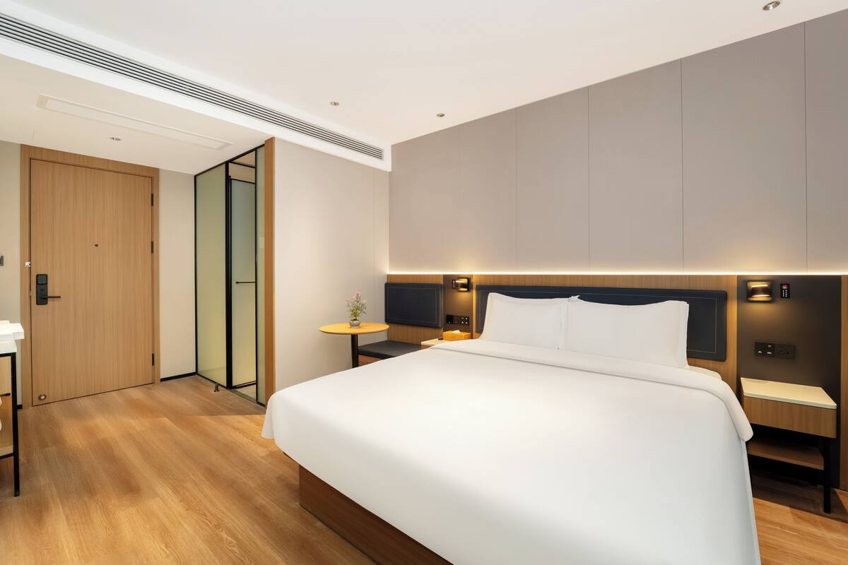 Una habitación de hotel moderna con una cama grande, mesitas de noche, un televisor y una puerta de madera.